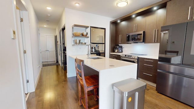 kitchen with sink, a kitchen bar, a kitchen island with sink, stainless steel appliances, and light hardwood / wood-style flooring