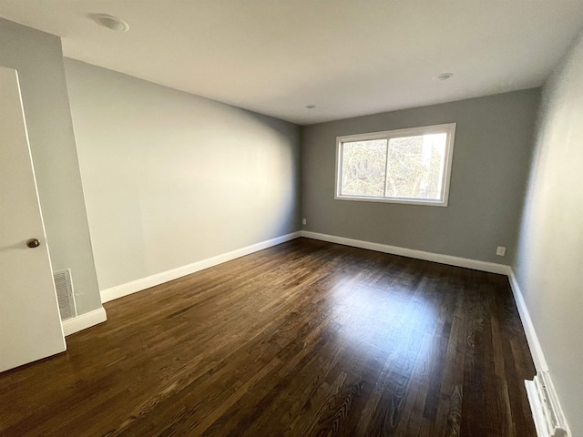 empty room with dark wood finished floors, visible vents, and baseboards