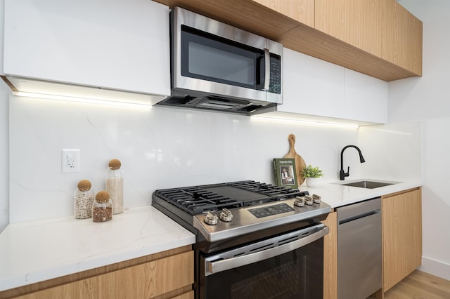 kitchen featuring appliances with stainless steel finishes, light hardwood / wood-style floors, light stone countertops, sink, and backsplash