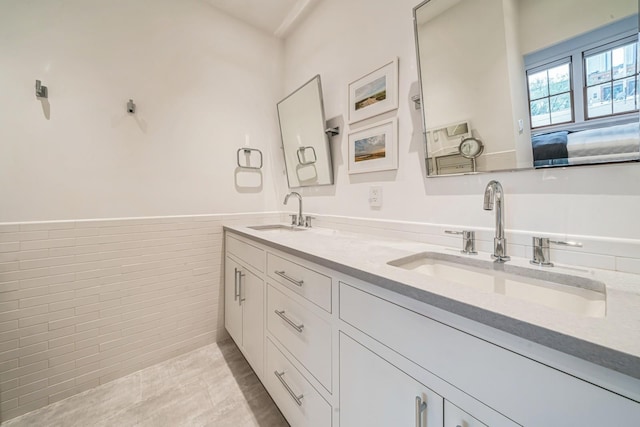 full bathroom with double vanity, a sink, and a wainscoted wall