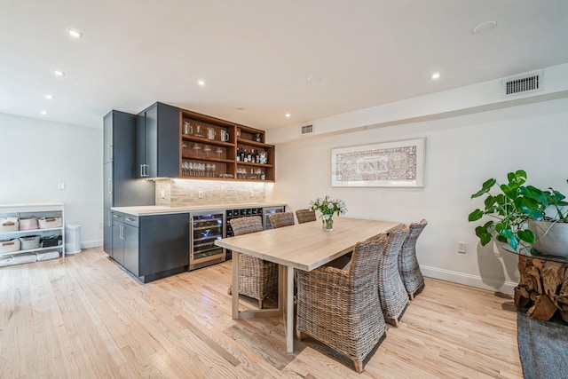 dining space featuring visible vents, baseboards, beverage cooler, a bar, and light wood finished floors