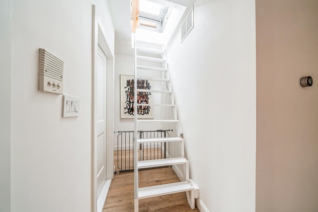 hall featuring a skylight, visible vents, baseboards, and light wood-type flooring