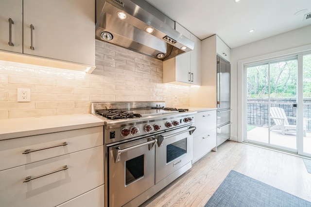 kitchen featuring wall chimney range hood, white cabinets, light countertops, light wood-style flooring, and premium appliances