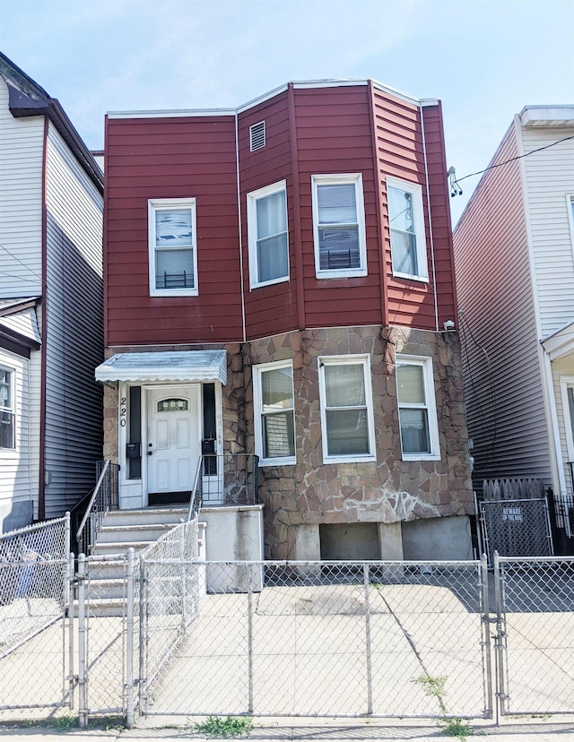 townhome / multi-family property featuring stone siding, a fenced front yard, and a gate