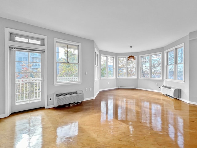 interior space with baseboard heating, a wall mounted AC, and light hardwood / wood-style flooring