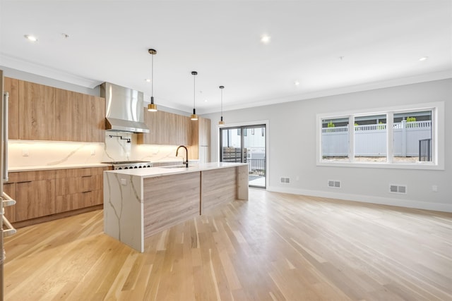 kitchen with visible vents, wall chimney exhaust hood, modern cabinets, a center island with sink, and pendant lighting