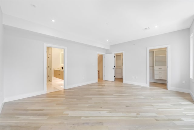 unfurnished bedroom featuring light wood-style flooring, connected bathroom, a spacious closet, and baseboards