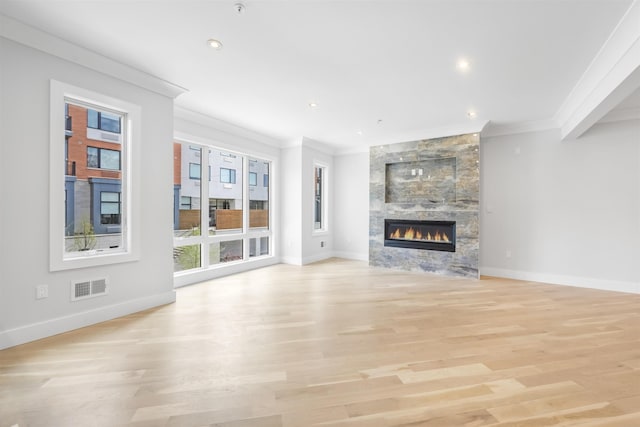 unfurnished living room with a fireplace, visible vents, ornamental molding, light wood-style floors, and baseboards