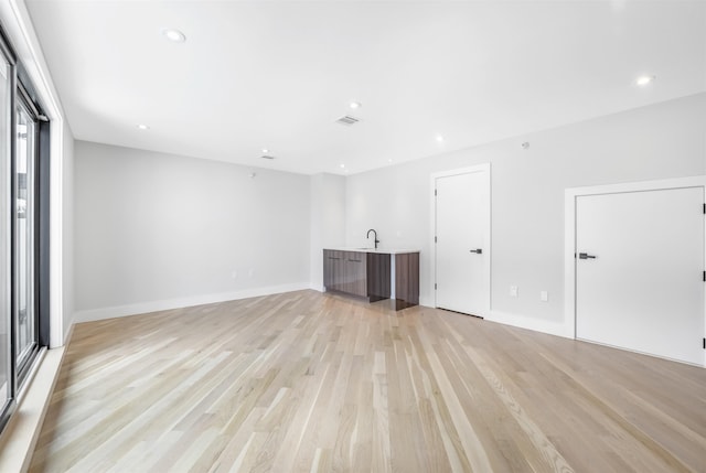 unfurnished living room featuring light wood-style floors, visible vents, a sink, and recessed lighting