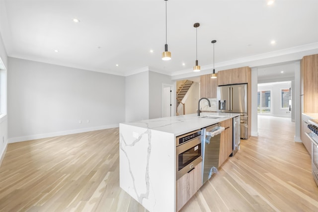 kitchen featuring a large island, stainless steel appliances, hanging light fixtures, a sink, and light stone countertops