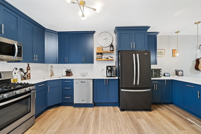 kitchen featuring pendant lighting, blue cabinetry, appliances with stainless steel finishes, tasteful backsplash, and light hardwood / wood-style floors