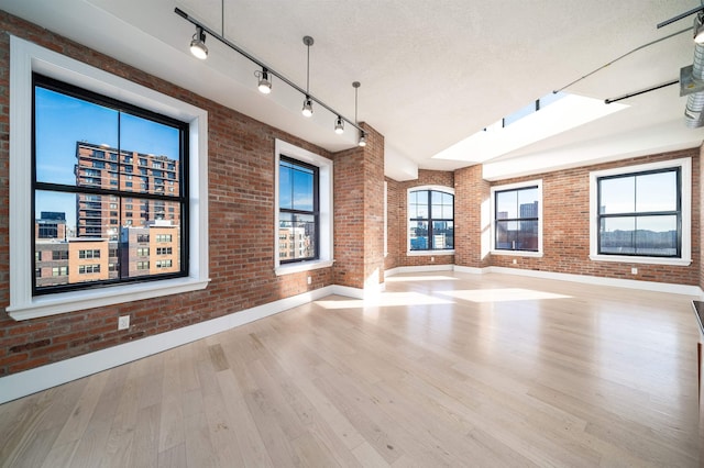 unfurnished room with light hardwood / wood-style floors, brick wall, and a textured ceiling