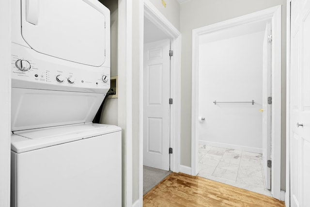 laundry area featuring stacked washer / dryer, laundry area, baseboards, and marble finish floor