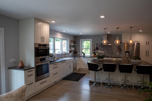 kitchen with dark countertops, a kitchen island, appliances with stainless steel finishes, white cabinetry, and a sink