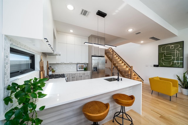 kitchen with kitchen peninsula, stainless steel refrigerator with ice dispenser, light wood-type flooring, sink, and hanging light fixtures