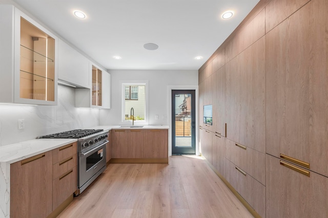 kitchen featuring light stone counters, high end stainless steel range, sink, white cabinets, and light hardwood / wood-style flooring