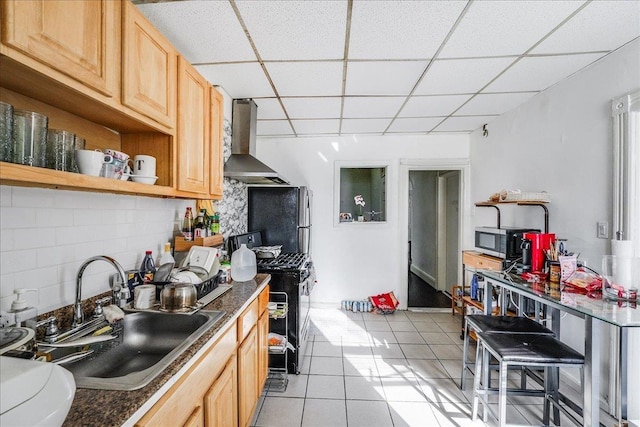 kitchen featuring gas stove, light brown cabinets, wall chimney range hood, a drop ceiling, and sink