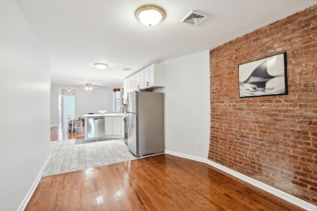 kitchen with white cabinetry, stainless steel appliances, brick wall, kitchen peninsula, and light hardwood / wood-style floors