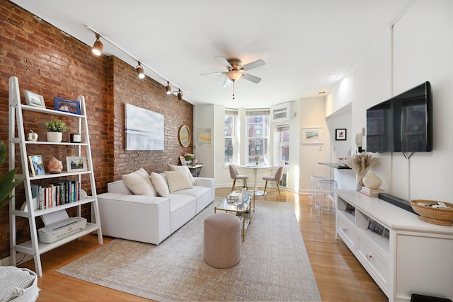 living room with track lighting, light wood-type flooring, brick wall, and ceiling fan