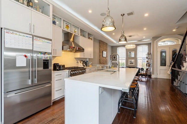 kitchen with high quality appliances, a kitchen island with sink, dark wood finished floors, wall chimney exhaust hood, and visible vents