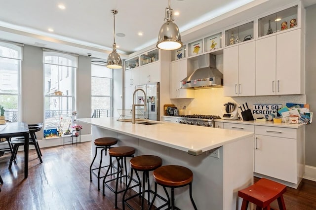 kitchen with a sink, wall chimney exhaust hood, an island with sink, and a wealth of natural light