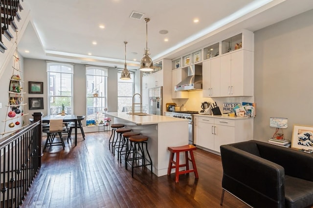 kitchen featuring wall chimney range hood, a sink, a breakfast bar, stainless steel appliances, and dark wood-type flooring