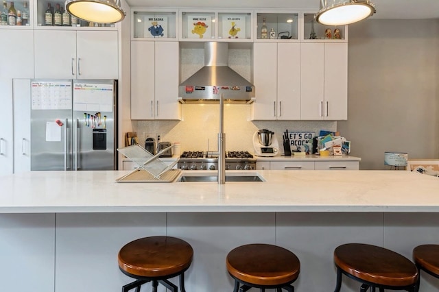 kitchen with stainless steel refrigerator with ice dispenser, white cabinetry, a breakfast bar, and wall chimney range hood