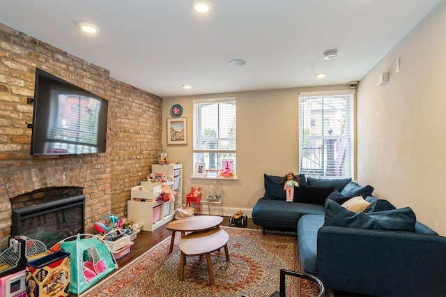 living area with brick wall, a fireplace, wood finished floors, baseboards, and recessed lighting