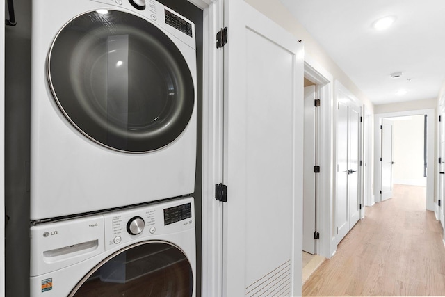 laundry room featuring stacked washing machine and dryer and light wood finished floors