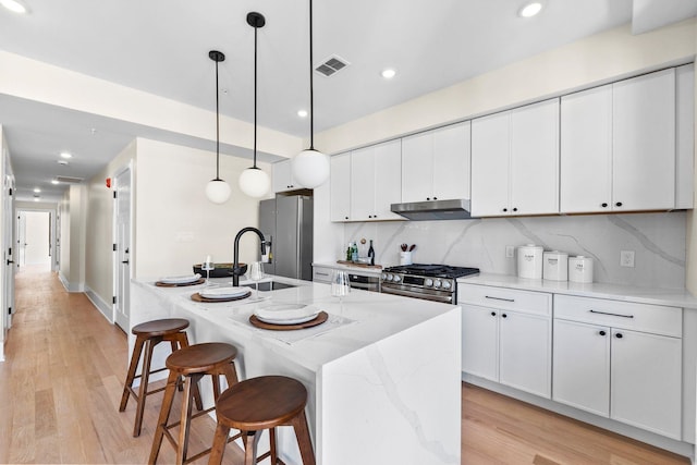 kitchen with appliances with stainless steel finishes, a kitchen bar, under cabinet range hood, white cabinetry, and recessed lighting