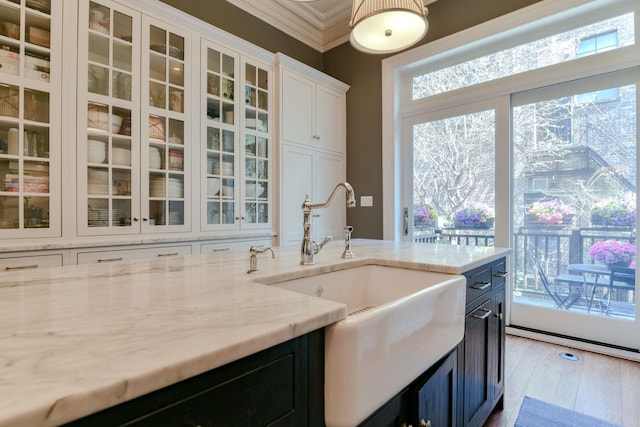 kitchen featuring crown molding, light stone counters, a sink, white cabinetry, and glass insert cabinets