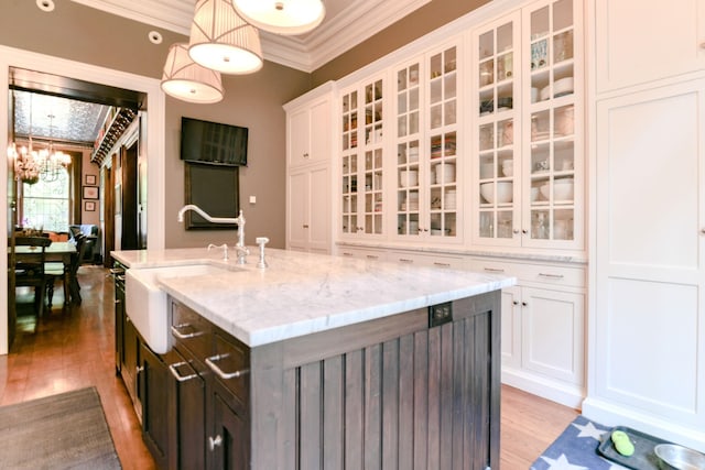 kitchen with crown molding, a sink, light wood-style floors, a chandelier, and white cabinetry