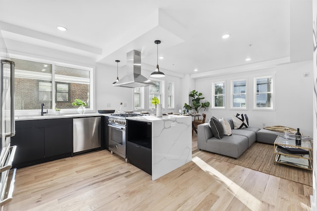 kitchen featuring island exhaust hood, a sink, dark cabinetry, a peninsula, and appliances with stainless steel finishes