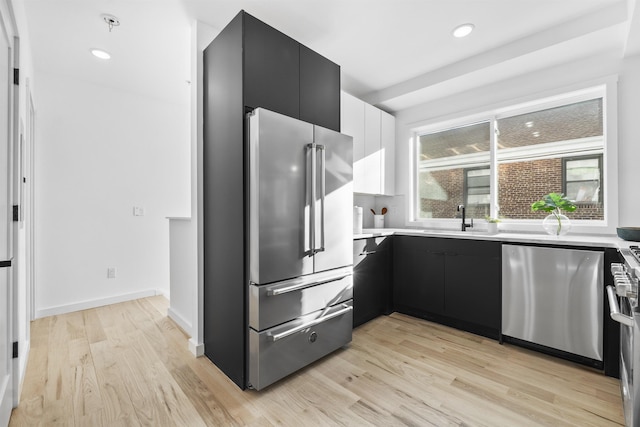 kitchen featuring light wood finished floors, stainless steel appliances, dark cabinetry, and modern cabinets