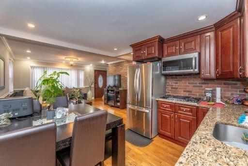 kitchen featuring light stone countertops, appliances with stainless steel finishes, light wood-type flooring, tasteful backsplash, and crown molding