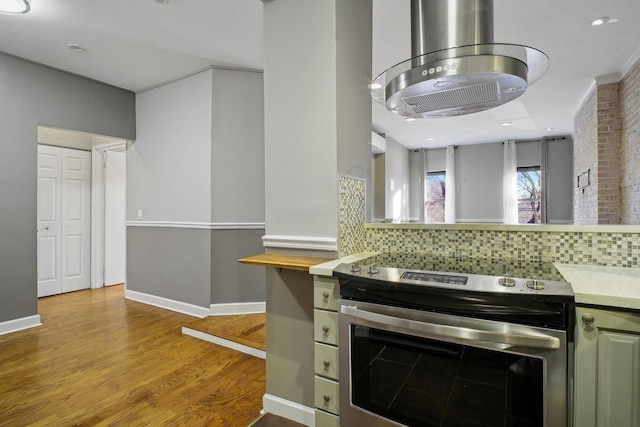 kitchen with light wood-type flooring, stainless steel electric range oven, backsplash, and brick wall