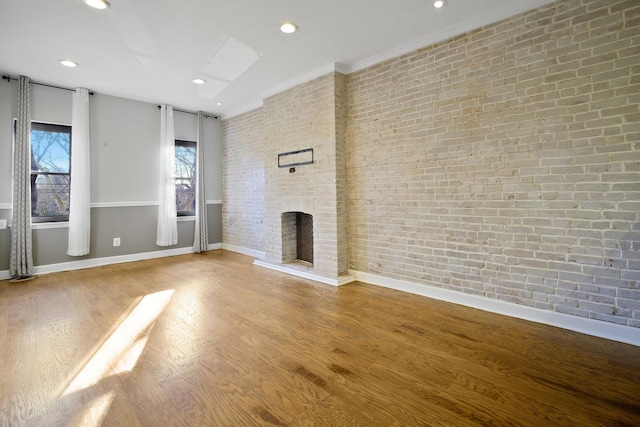 unfurnished living room with wood-type flooring, brick wall, and a brick fireplace