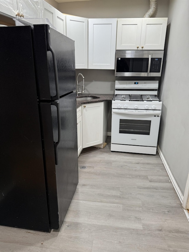 69 Jewett Ave, Jersey City, NJ 07304 - kitchen featuring stainless steel microwave, white gas range oven, freestanding refrigerator, a sink, and white cabinetry