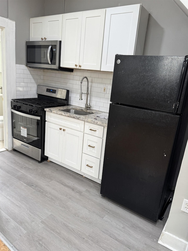 69 Jewett Ave, Jersey City, NJ 07304 - kitchen with stainless steel appliances, a sink, light wood-style floors, white cabinetry, and light stone counters