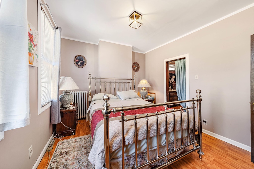 bedroom featuring ornamental molding, radiator heating unit, wood finished floors, and baseboards