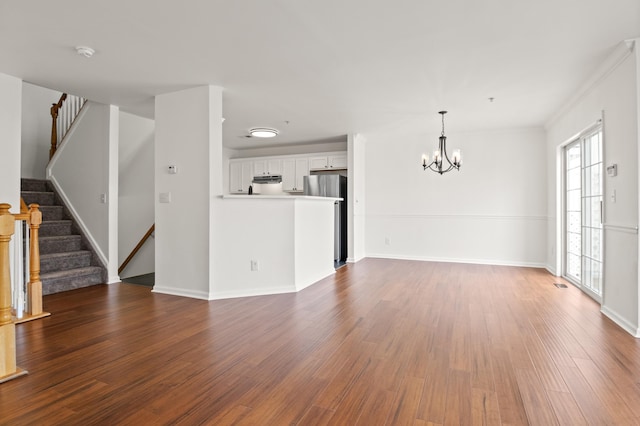 unfurnished living room with an inviting chandelier, dark wood-style flooring, stairs, and baseboards