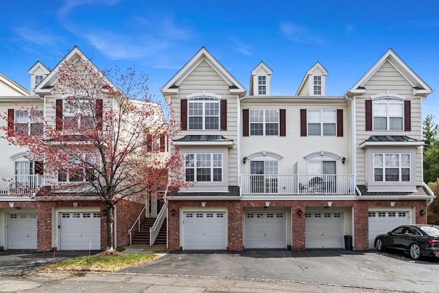 multi unit property featuring brick siding, an attached garage, driveway, and stairs