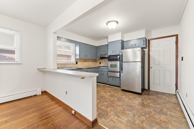 kitchen with kitchen peninsula, appliances with stainless steel finishes, backsplash, and a baseboard radiator