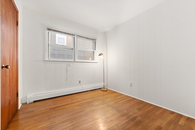 unfurnished room with a baseboard radiator, light hardwood / wood-style floors, and wood walls