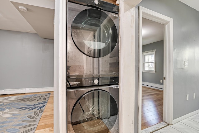 washroom with stacked washing maching and dryer, a baseboard heating unit, and light hardwood / wood-style floors