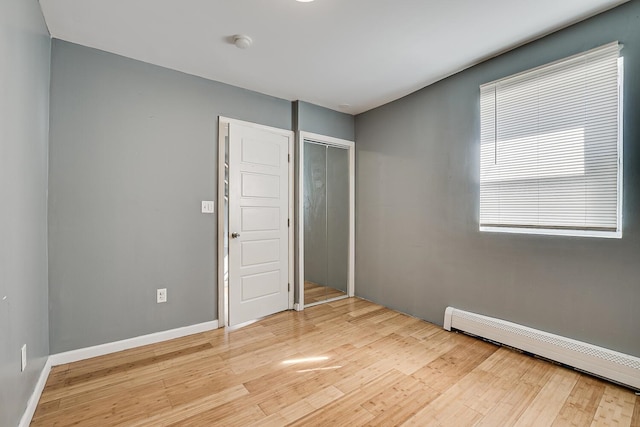 unfurnished bedroom featuring baseboard heating, light wood-type flooring, and a closet