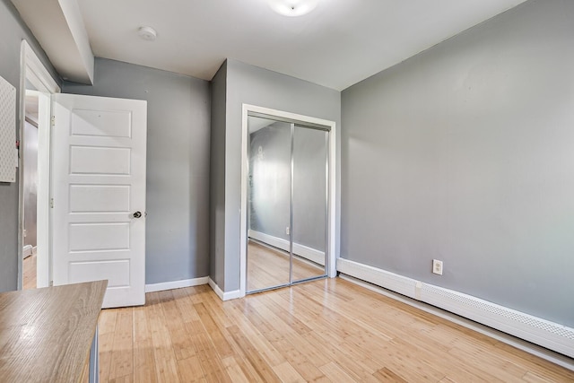 unfurnished bedroom with a closet, light hardwood / wood-style floors, and a baseboard heating unit