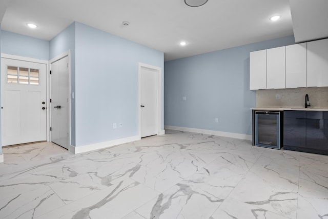 unfurnished living room featuring a sink, baseboards, marble finish floor, wine cooler, and recessed lighting