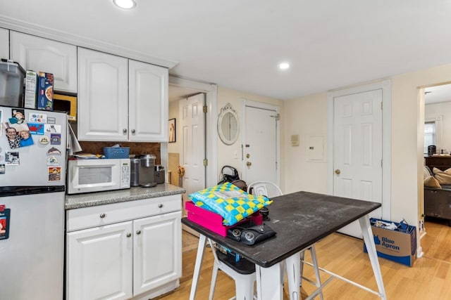 kitchen with a breakfast bar, backsplash, white appliances, light hardwood / wood-style flooring, and white cabinets