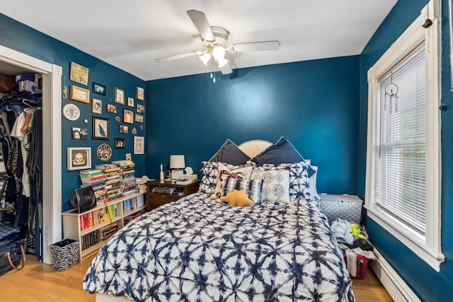 bedroom featuring a baseboard heating unit, hardwood / wood-style floors, ceiling fan, and a closet